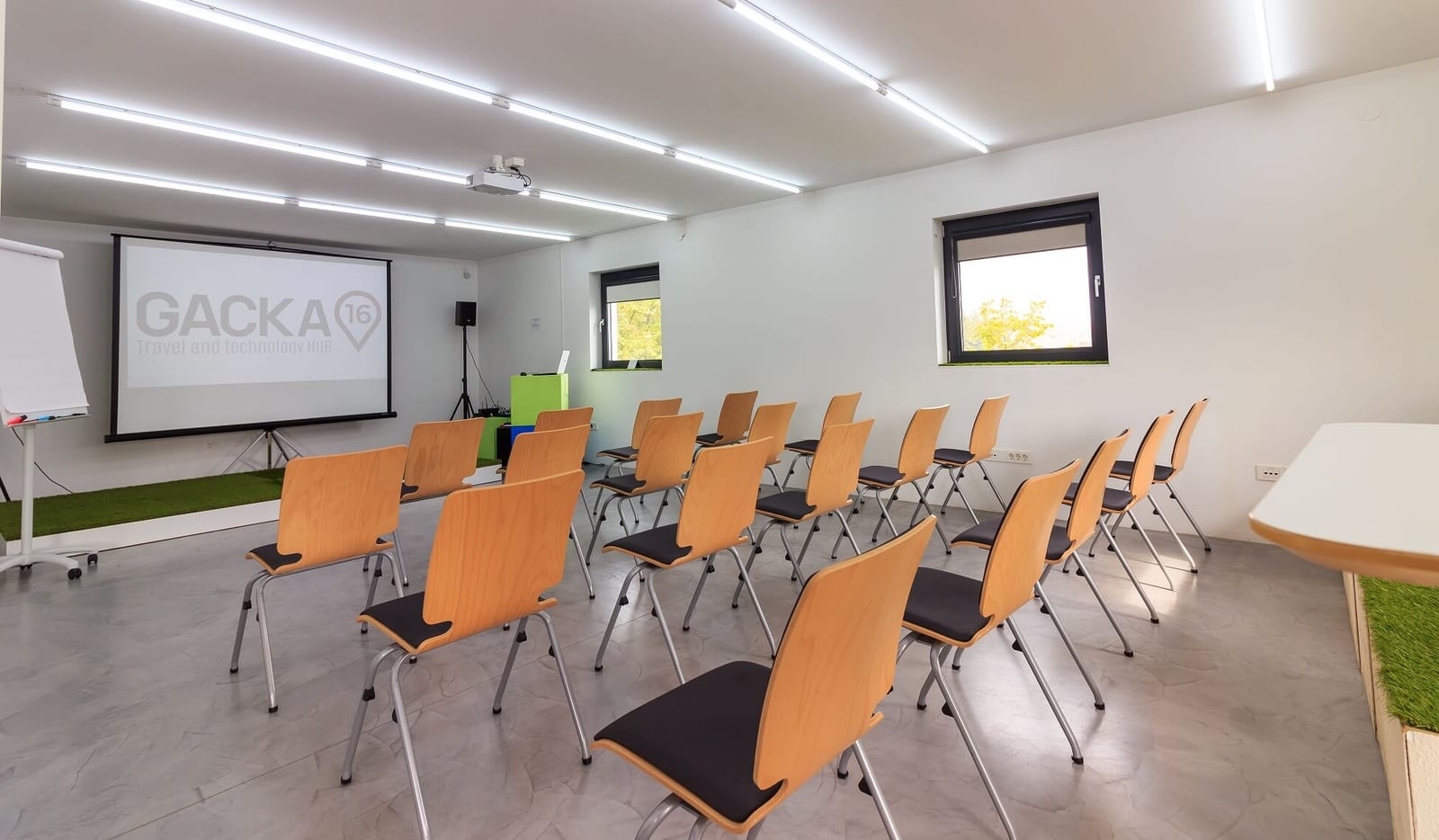 Redovi drvenih stolica s crnim sjedalima ispred platna za projekciju