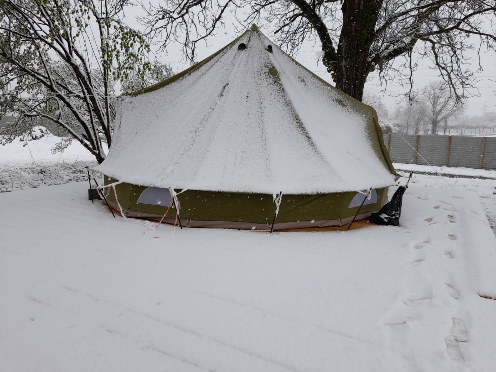 Olive bell tent covered in snow with footprints in the snow around it