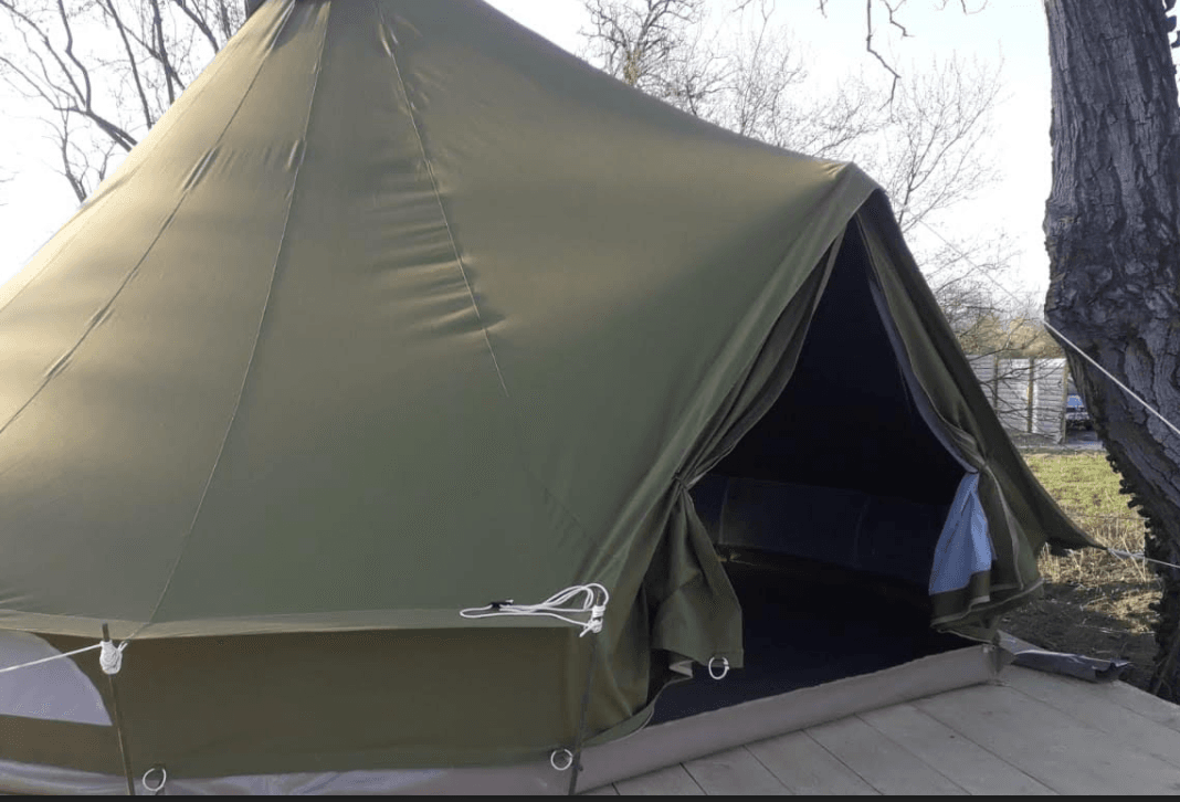 Olive bell tent with its door open on a wooden deck among bare trees
