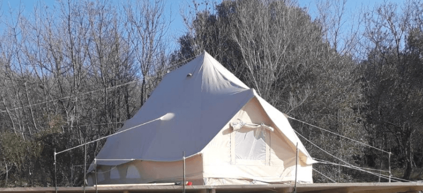 Cream bell tent on a wooden deck before bare trees and a clear sky