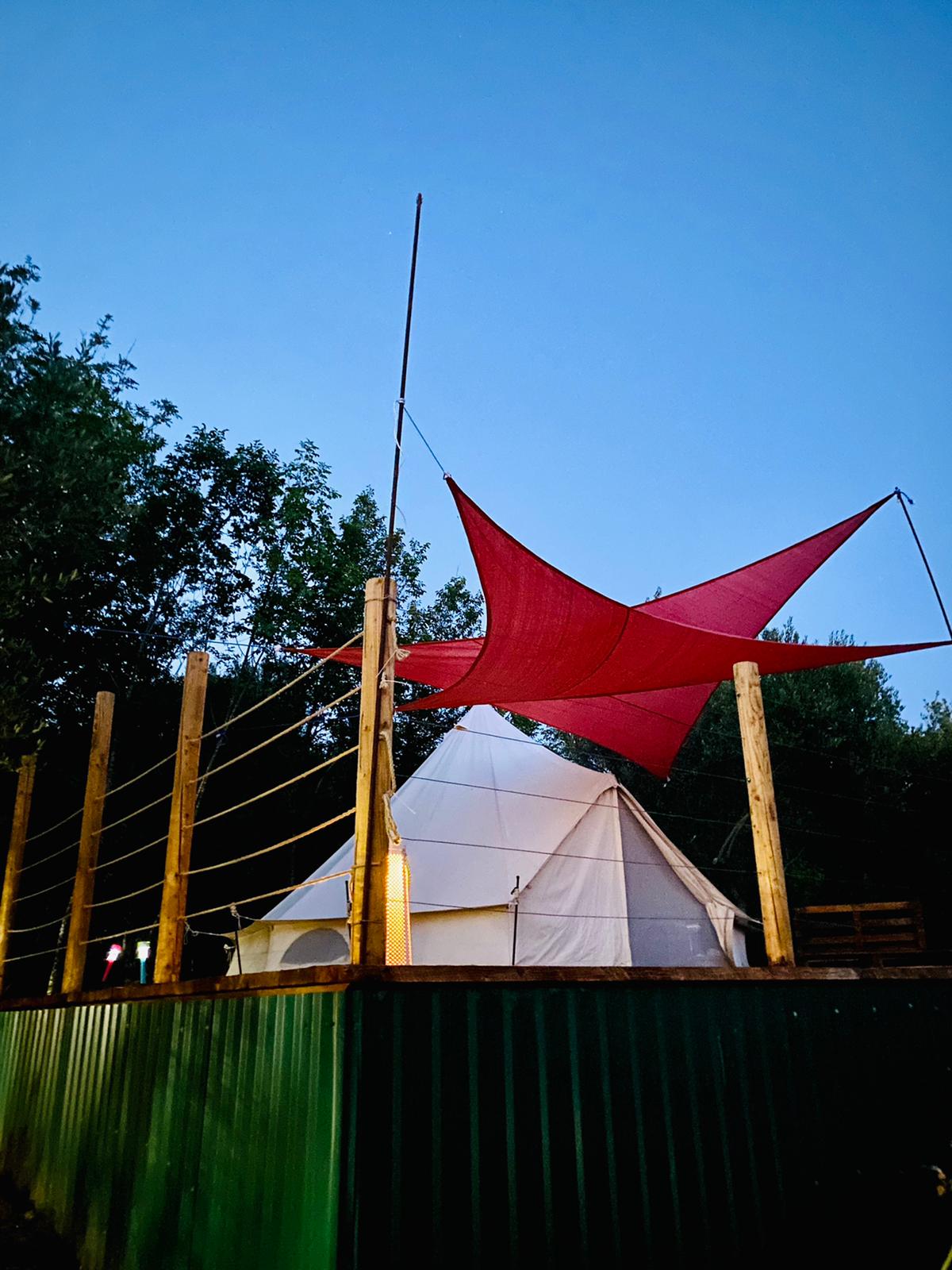 Red shade sail stretched above the cream tent at dusk