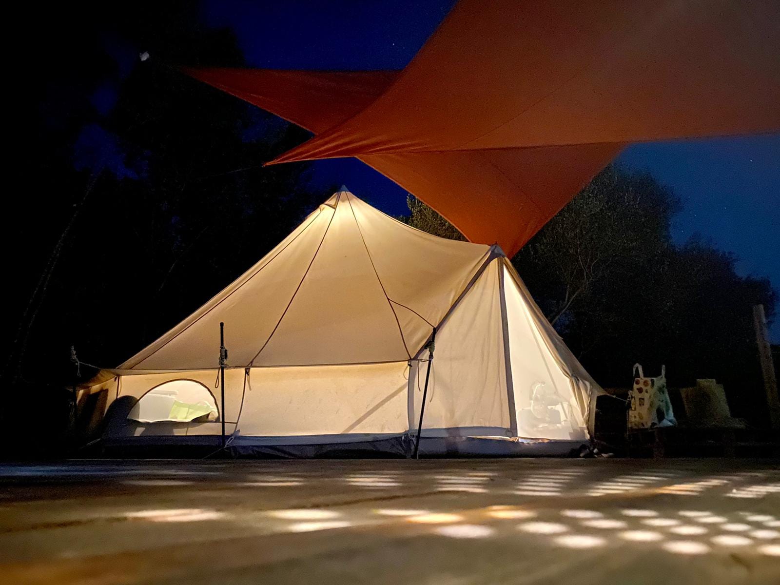Lit tent at dusk beneath the coral shade sail