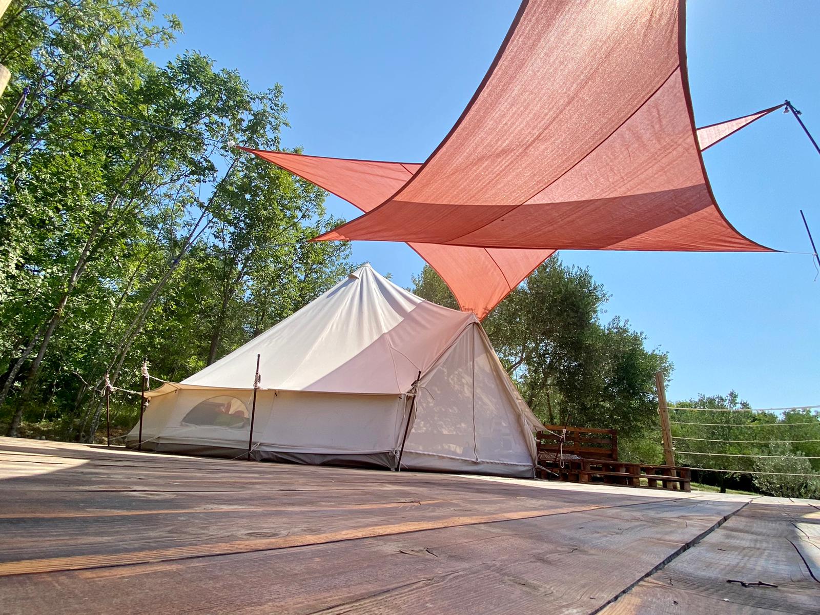 Cream bell tent on a wide wooden deck under a coral shade sail